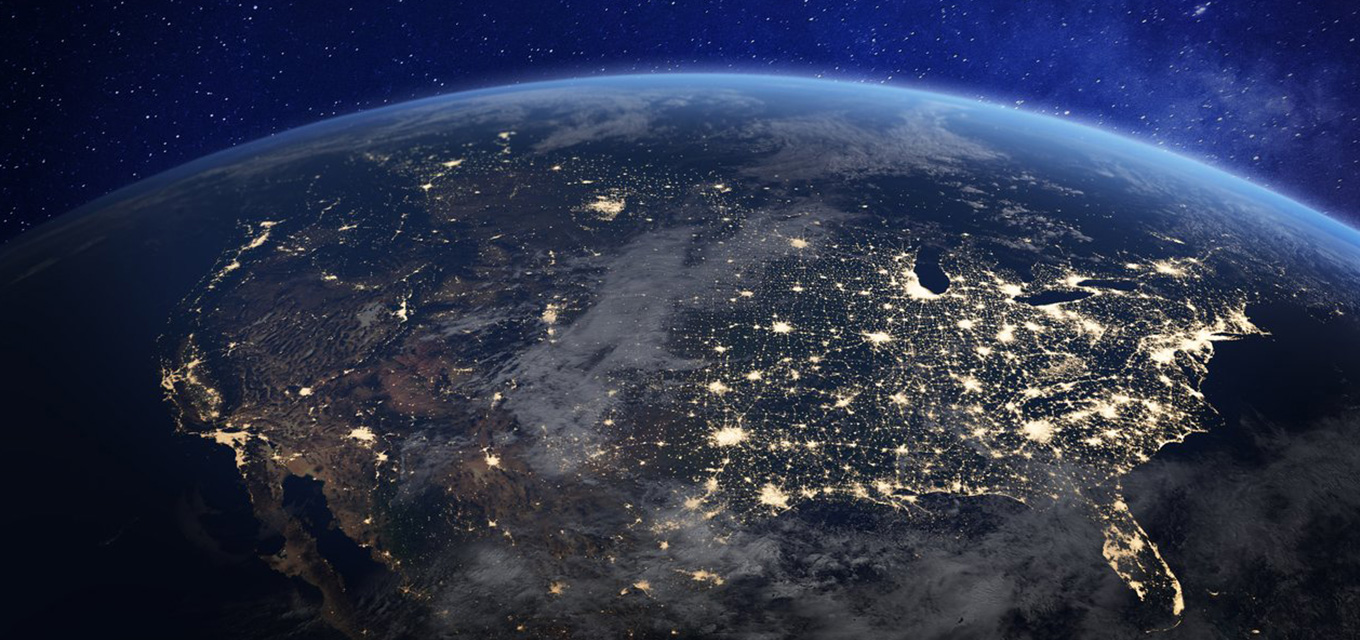 View of Earth from space at night, showing illuminated city lights across North America under a dark blue sky.